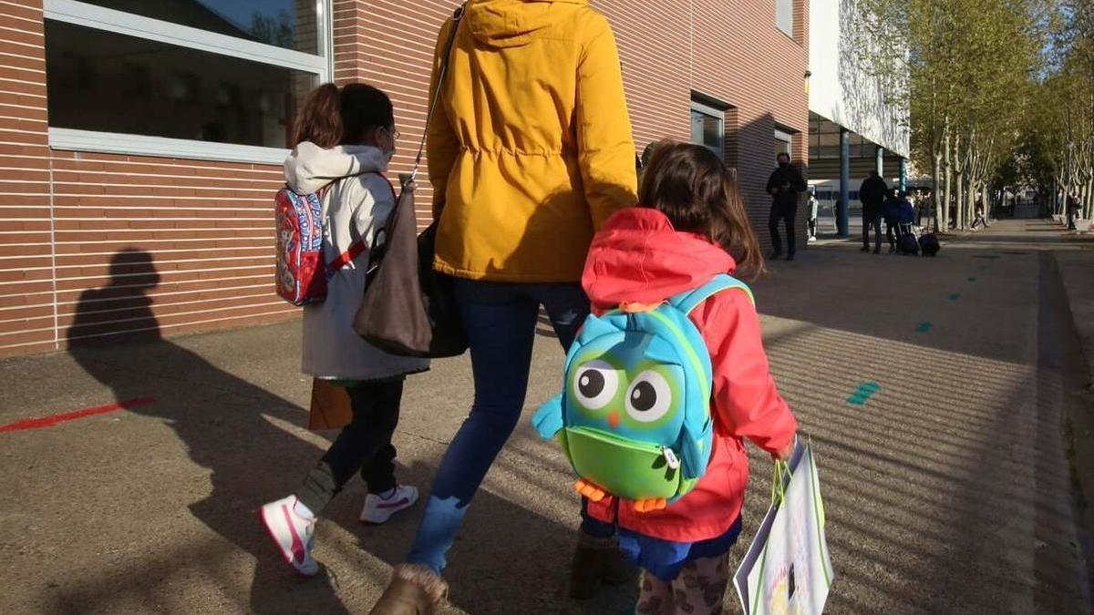 Una madre camina con sus hijas hacia la escuela.