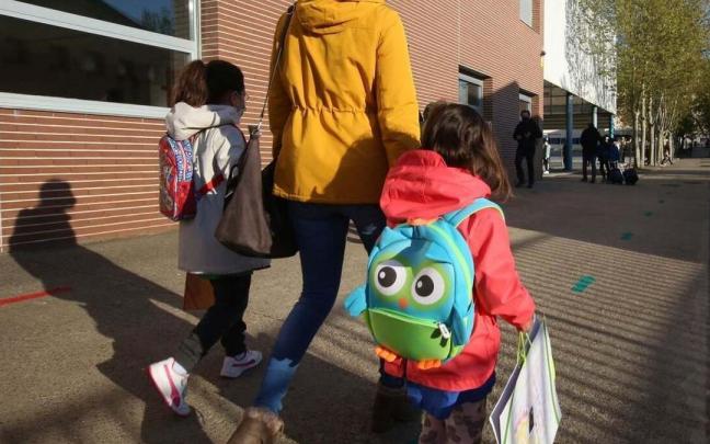 Una madre camina con sus hijas hacia la escuela.