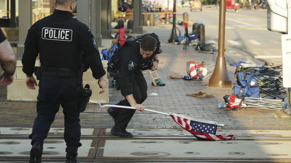 Un policía recoge una bandera de EEUU en la escena donde Robert Crimo disparó durante el desfile del 4 de julio en Highland Park.