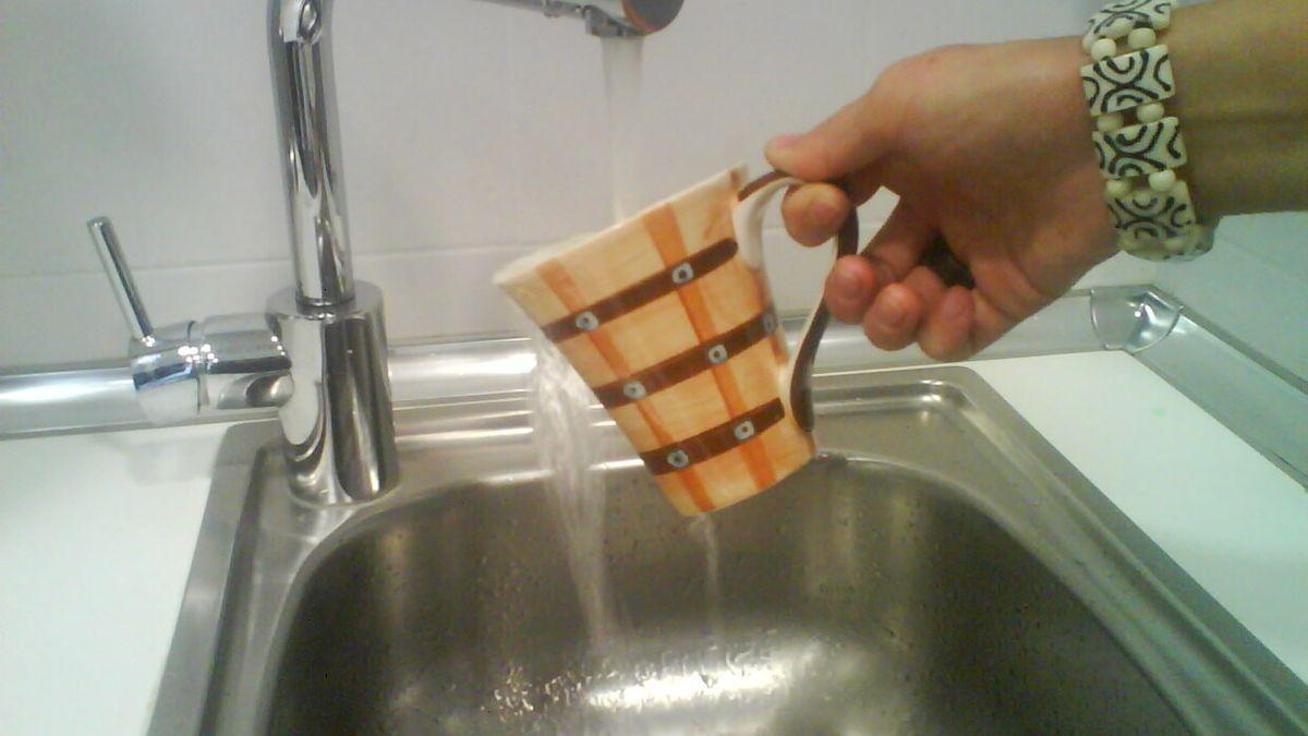 Una mujer llena una taza de agua del grifo.