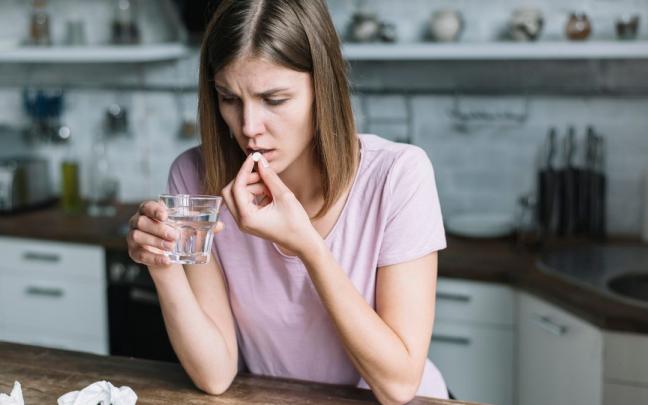 Una mujer se mete una pastilla en la boca.
