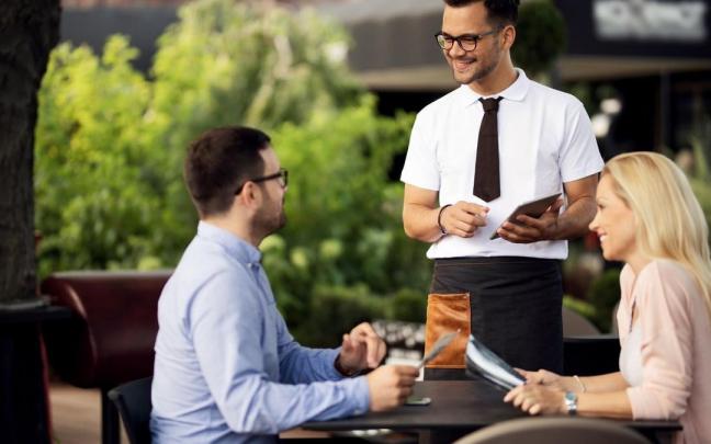 Un camarero atendiendo con un comandero digital a los clientes.