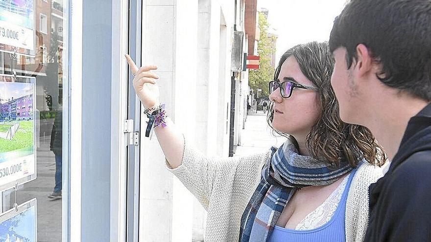 Dos jóvenes consultan ofertas de vivienda en el escaparate de una inmobiliaria.