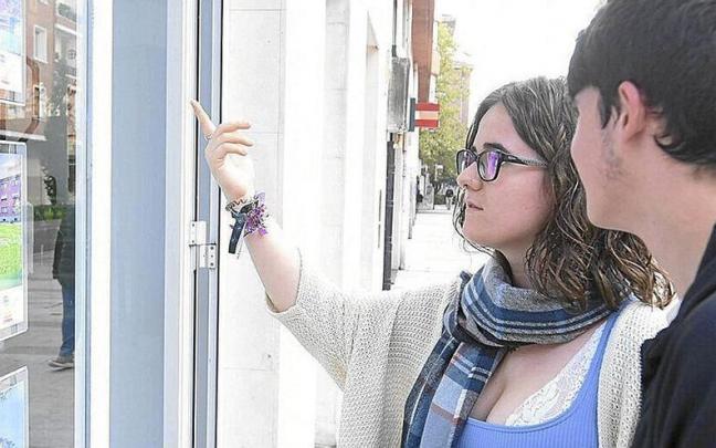 Dos jóvenes consultan ofertas de vivienda en el escaparate de una inmobiliaria. Dos jóvenes consultan ofertas de vivienda en el escaparate de una inmobiliaria.