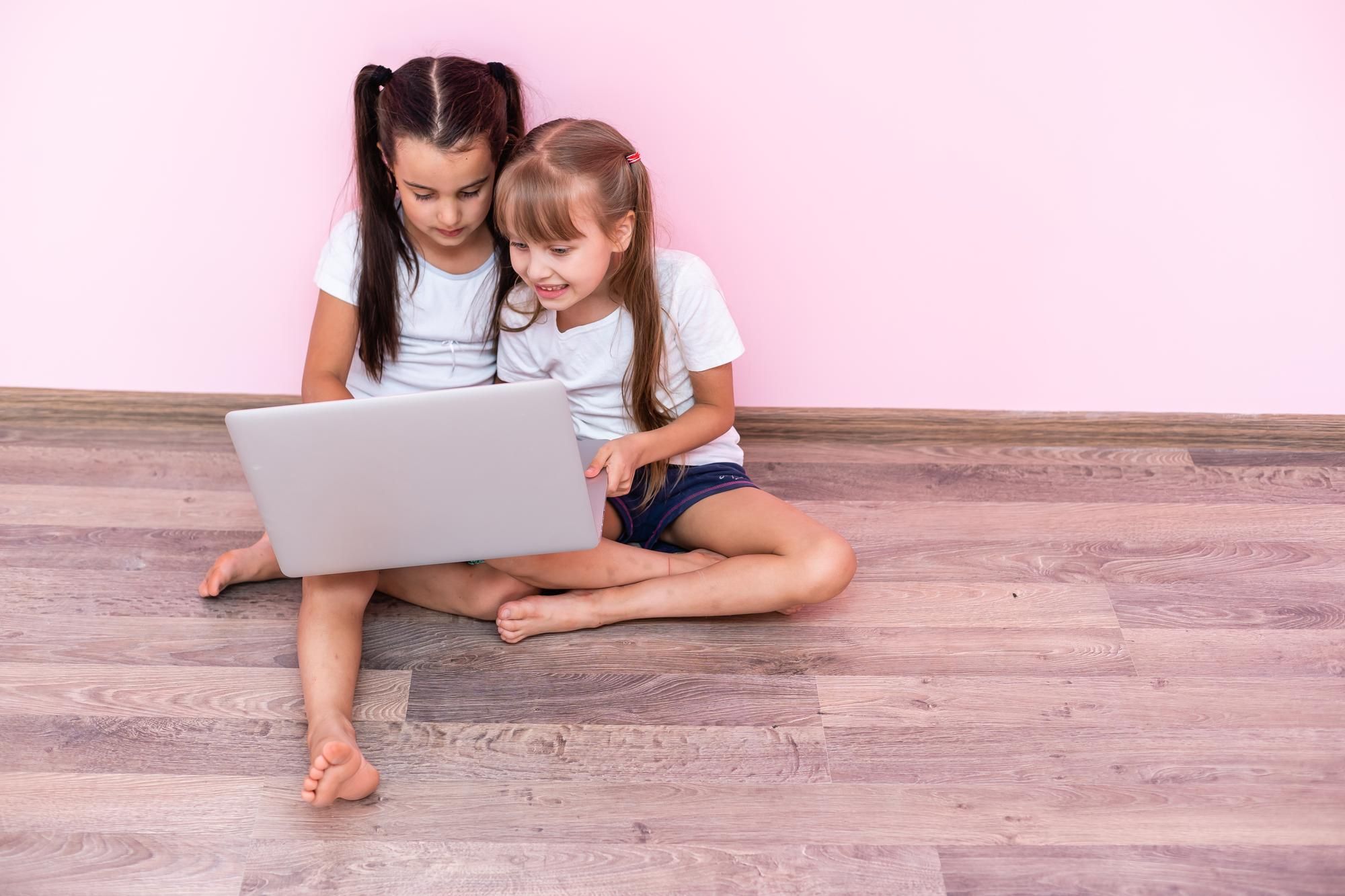 Dos niñas juegan con una tablet sentadas en el suelo.