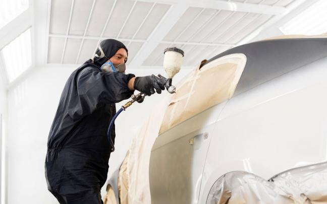 Un hombre pinta la carrocer&iacute;a de un coche.