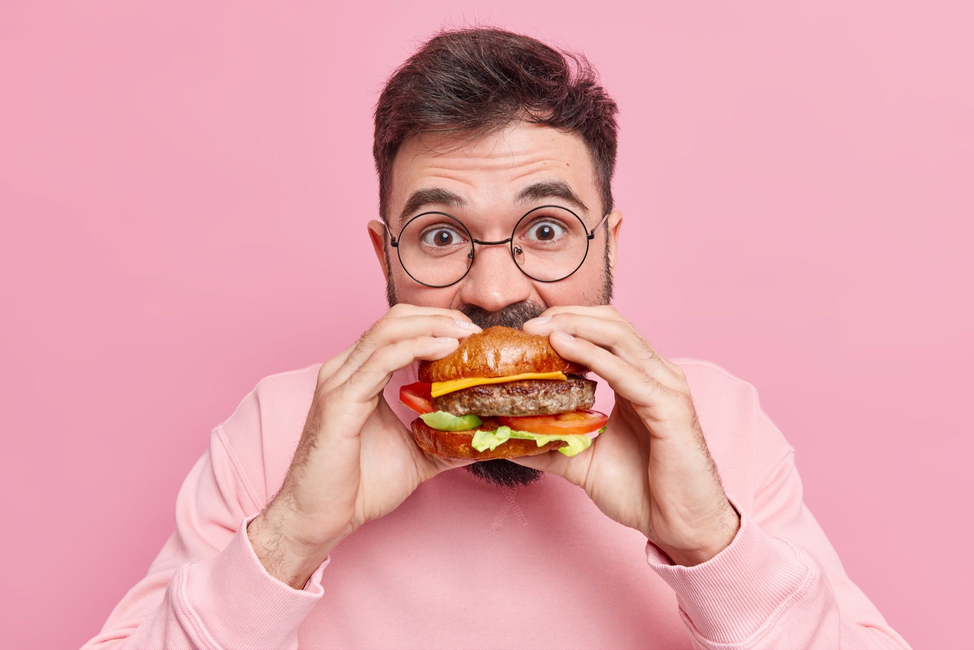 Un hombre come con ansiedad una hamburguesa.