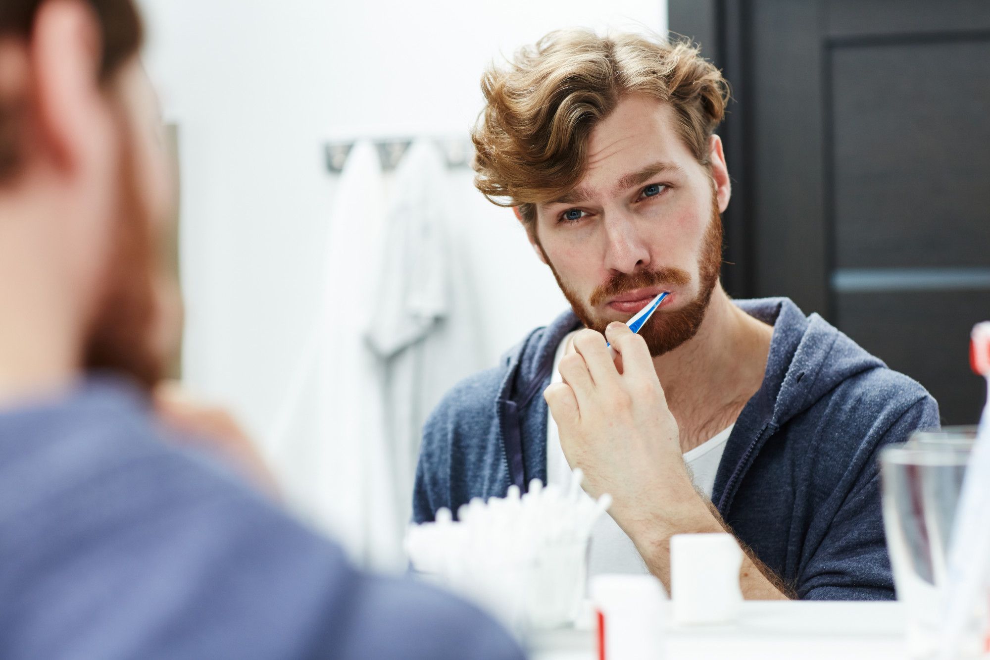 Un hombre se lava los dientes frente a un espejo.