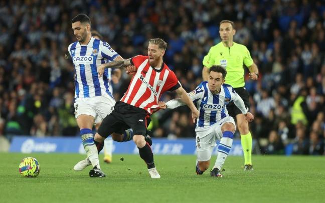 Mart&iacute;n Zubimendi agarra a Iker Muniain mientras este trata de arrebatarle el bal&oacute;n a Mikel Merino.