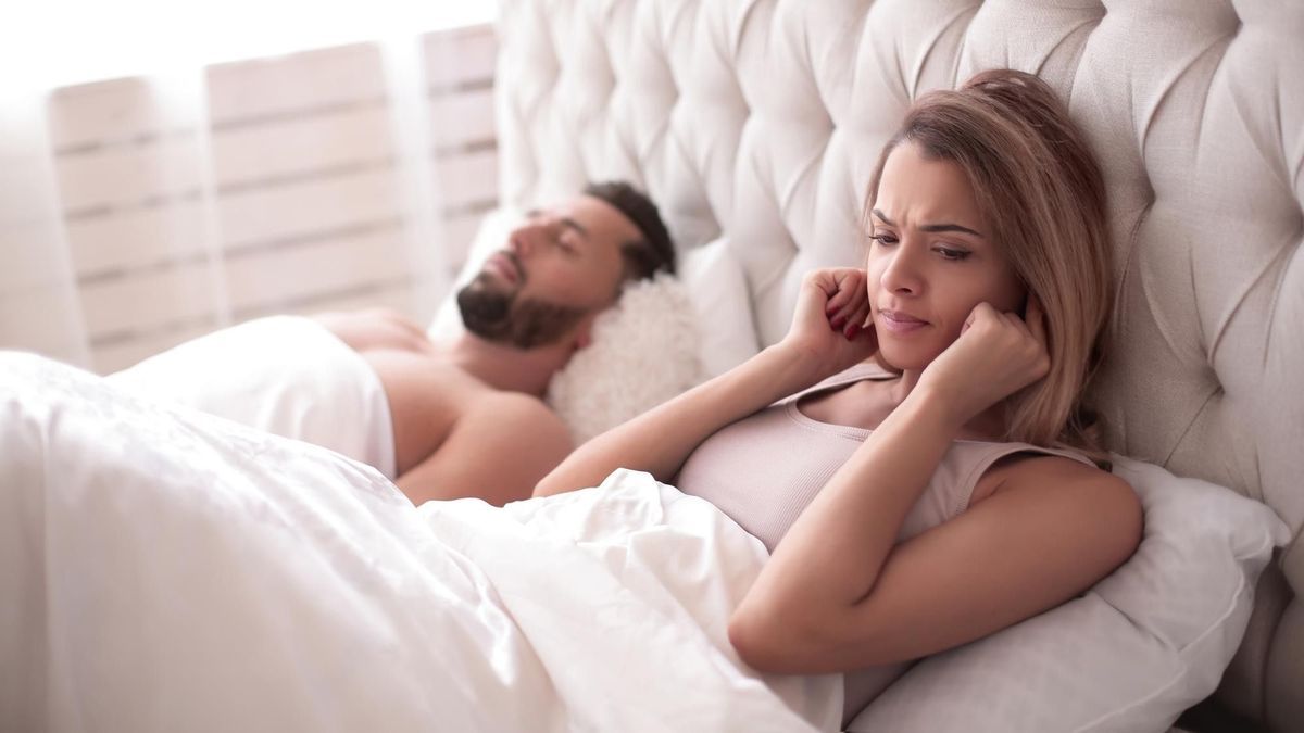 Una mujer se tapa los oídos mientras su marido duerme.