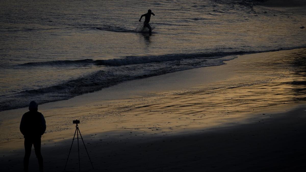 Un hombre fotografía el amanecer en la playa donostiarra de Ondarreta, este jueves, mientras otro se baña