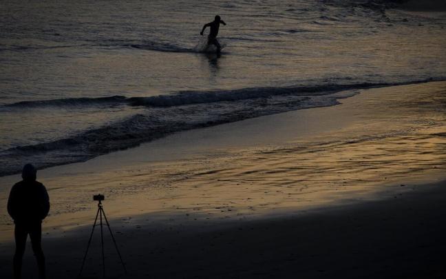 Un hombre fotografía el amanecer en la playa donostiarra de Ondarreta, este jueves, mientras otro se baña Un hombre fotografía el amanecer en la playa donostiarra de Ondarreta, este jueves, mientras otro se baña
