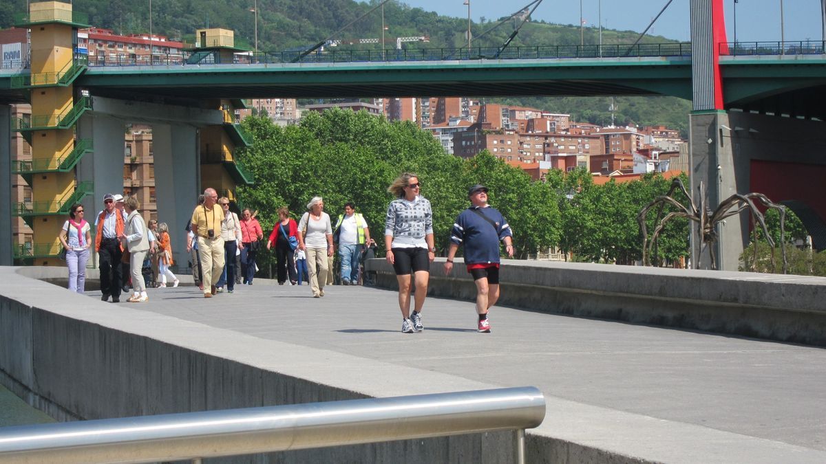 Varios turistas pasean junto a la ría de Bilbao.