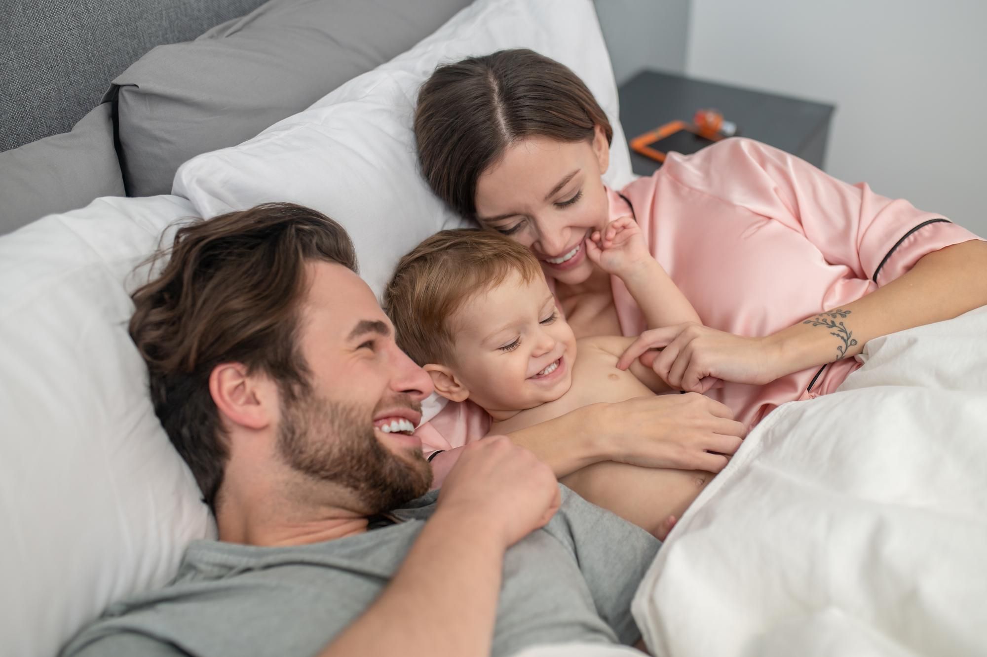 Una pareja ríe con su bebé en la cama.