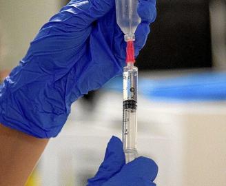 Un profesional sanitario rellenando en Vitoria la jeringuilla con la que va a administrar la vacuna contra el coronavirus. En la otra página, cartel indicador de Urgencias, en el exterior del Hospital Universitario Araba (HUA)-Txagorritxu, de la capital a