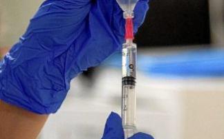 Un profesional sanitario rellenando en Vitoria la jeringuilla con la que va a administrar la vacuna contra el coronavirus. En la otra página, cartel indicador de Urgencias, en el exterior del Hospital Universitario Araba (HUA)-Txagorritxu, de la capital a