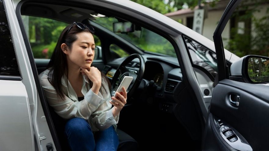 Mujer joven ojea su móvil sentada en el asiento delantero de un coche estacionado.
