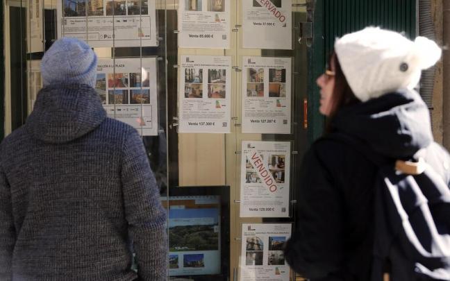 Jóvenes observan ofertas de alquiler y venta de viviendas en el escaparate de una inmobiliaria. Jóvenes observan ofertas de alquiler y venta de viviendas en el escaparate de una inmobiliaria.