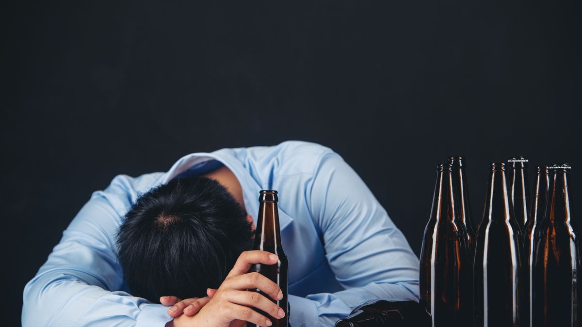 Un hombre con problemas de alcoholismo se derrumba encima de una mesa.