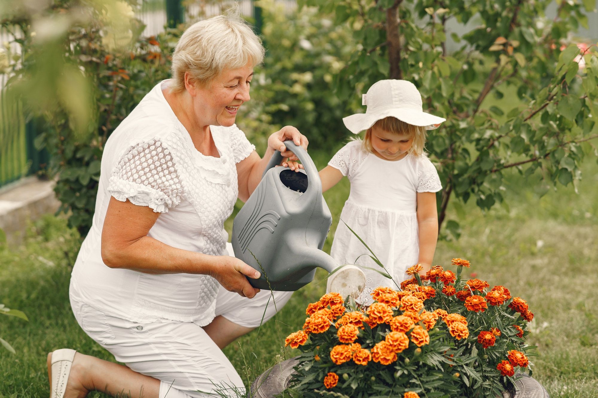 Una niña ayuda a su abuela a regar las flores del jardín.