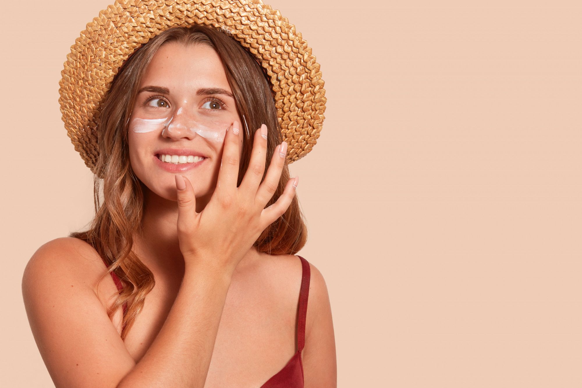 Una mujer se da crema solar protegida por un gorro.
