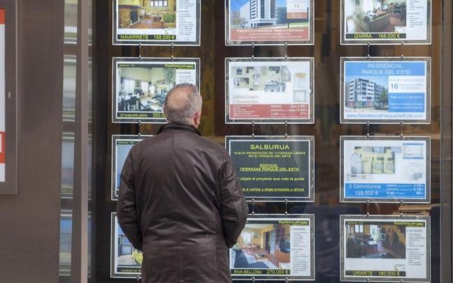 Un hombre mirando un escaparate con las ofertas de pisos en venta y alquiler de una inmobiliaria