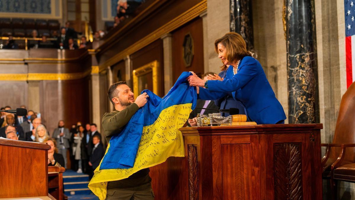 El presidente de Ucrania, Volodimir Zelenski, entrega a la presidenta de la Cámara de Representantes de Estados Unidos, Nancy Pelosi, una bandera de Ucrania.