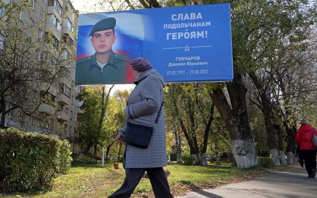 Una mujer camina por las calles de Mosc&uacute; junto a un cartel con la imagen de un soldado ruso ca&iacute;do en Ucrania.