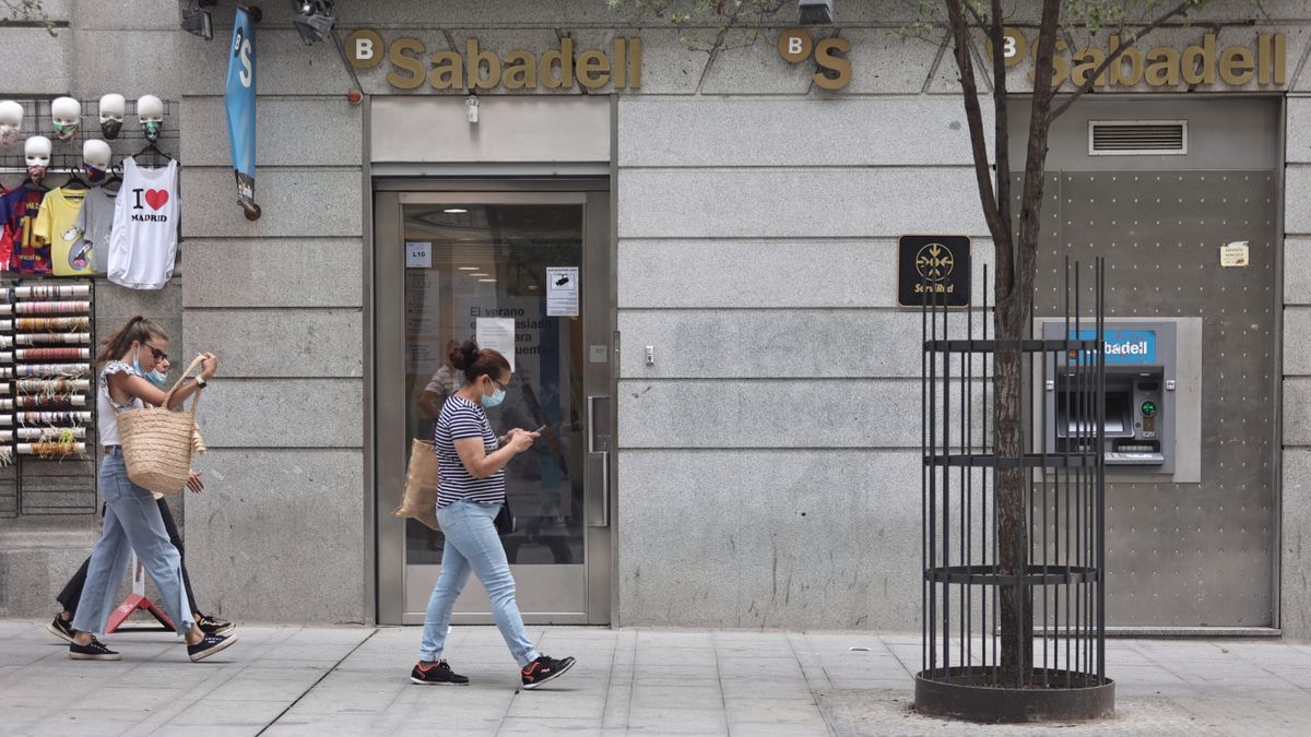 Dos mujeres pasan por una sucursal de banco Sabadell.
