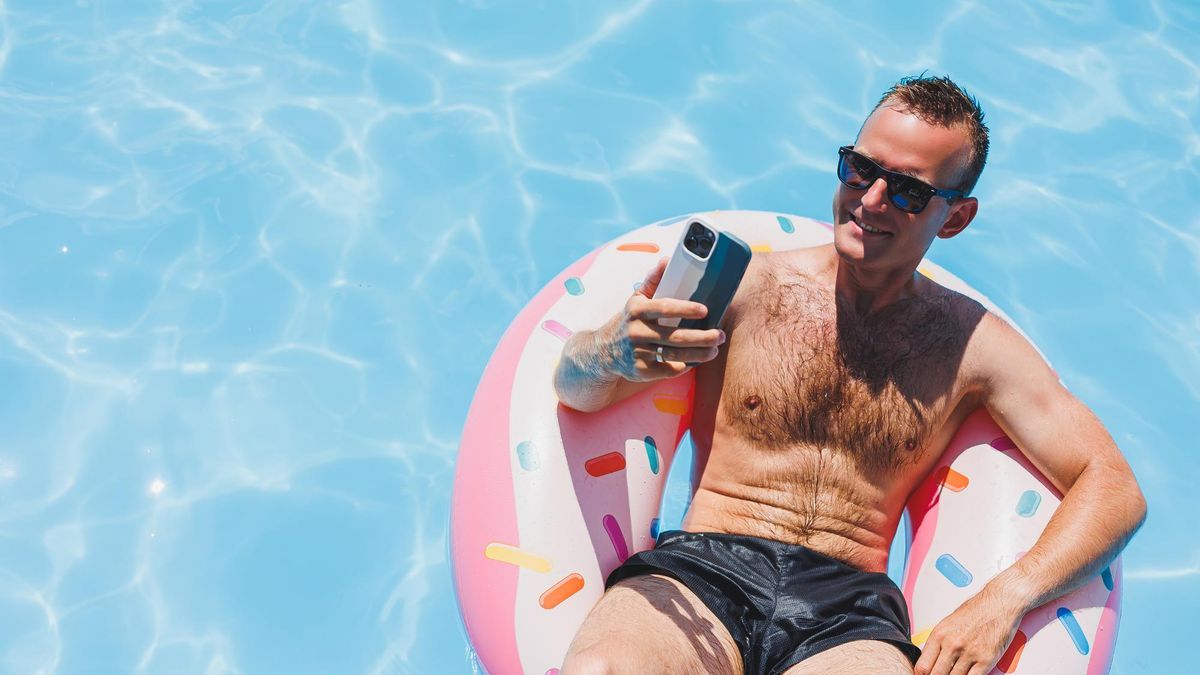 Un hombre sostiene el móvil sentado en un flotador en una piscina.