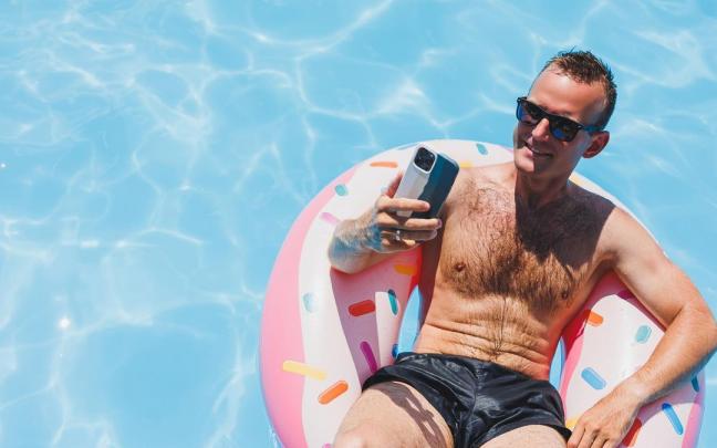 Un hombre sostiene el móvil sentado en un flotador en una piscina. Un hombre sostiene el móvil sentado en un flotador en una piscina.