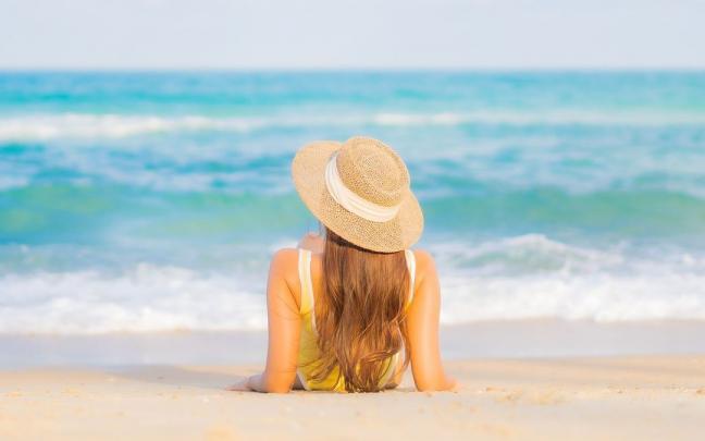 Una mujer toma el sol en la playa sentada sobre la arena.