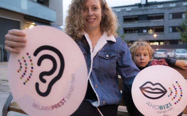 Marta Trigo, bere seme Xoanekin, Euskaraldiko 'ahobizi' eta 'belarriprest' rolak irudikatzen dituzten bi kartel eskuan dituela.