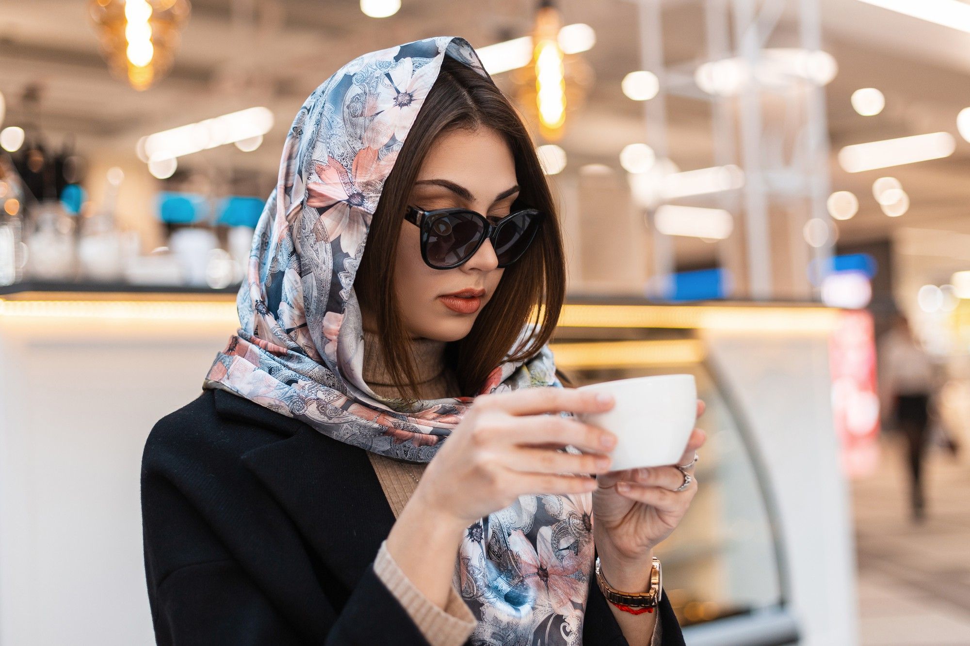 Una mujer con un fular por la cabeza toma un café en la cafetería de un aeropuerto.