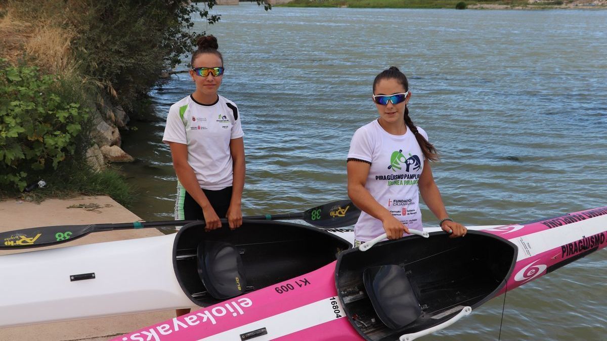 Ainé y Danae Sanmartín posan con sus piraguas en el embarcadero de Tudela, con el río Ebro al fondo.