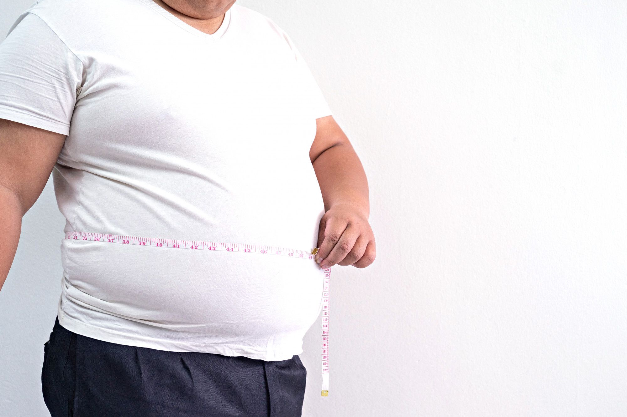 Un hombre obeso mide su abdomen con una cinta métrica.