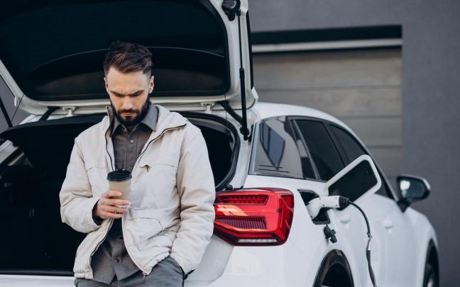 Un hombre toma un café mientras espera a que se cargue su coche. Un hombre toma un café mientras espera a que se cargue su coche.