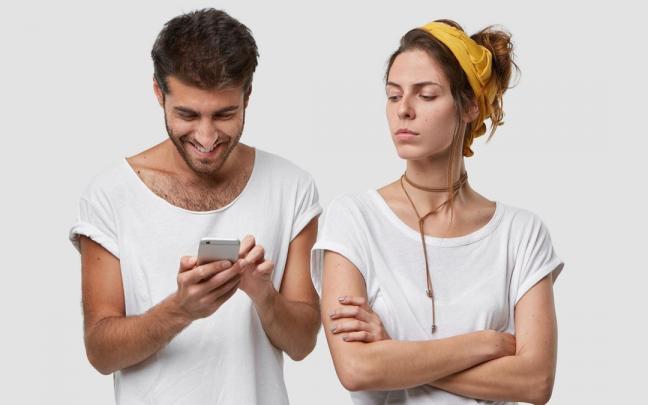 Una mujer mira a su pareja con cara de disgusto mientras este escribe en el móvil. Una mujer mira a su pareja con cara de disgusto mientras este escribe en el móvil.