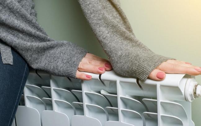 Una mujer se calienta las manos en un radiador.