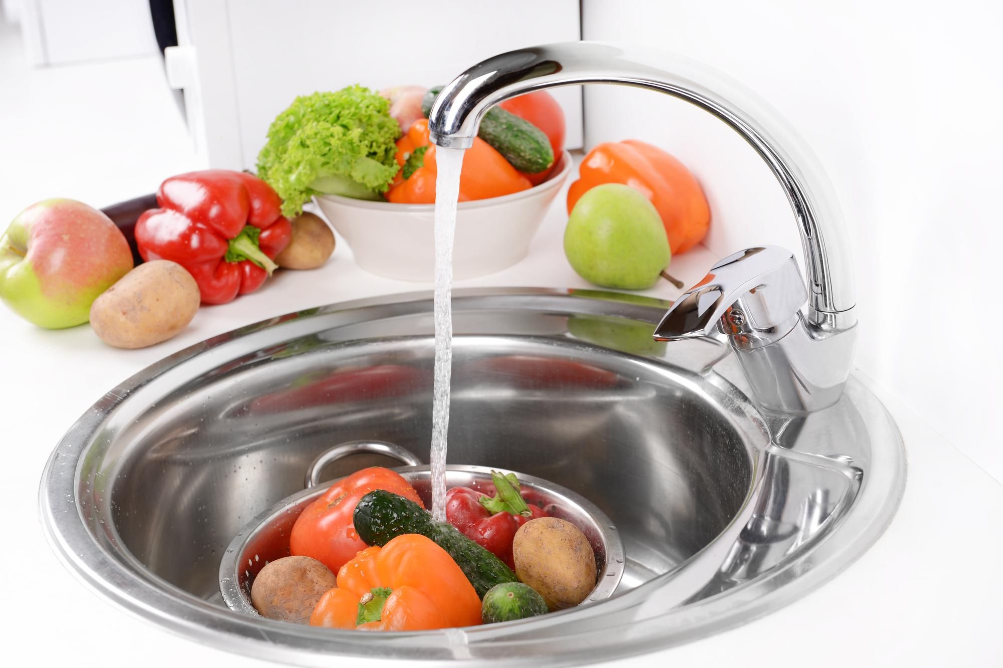 Frutas y verduras bajo el chorro de agua del grifo en un fregadero.