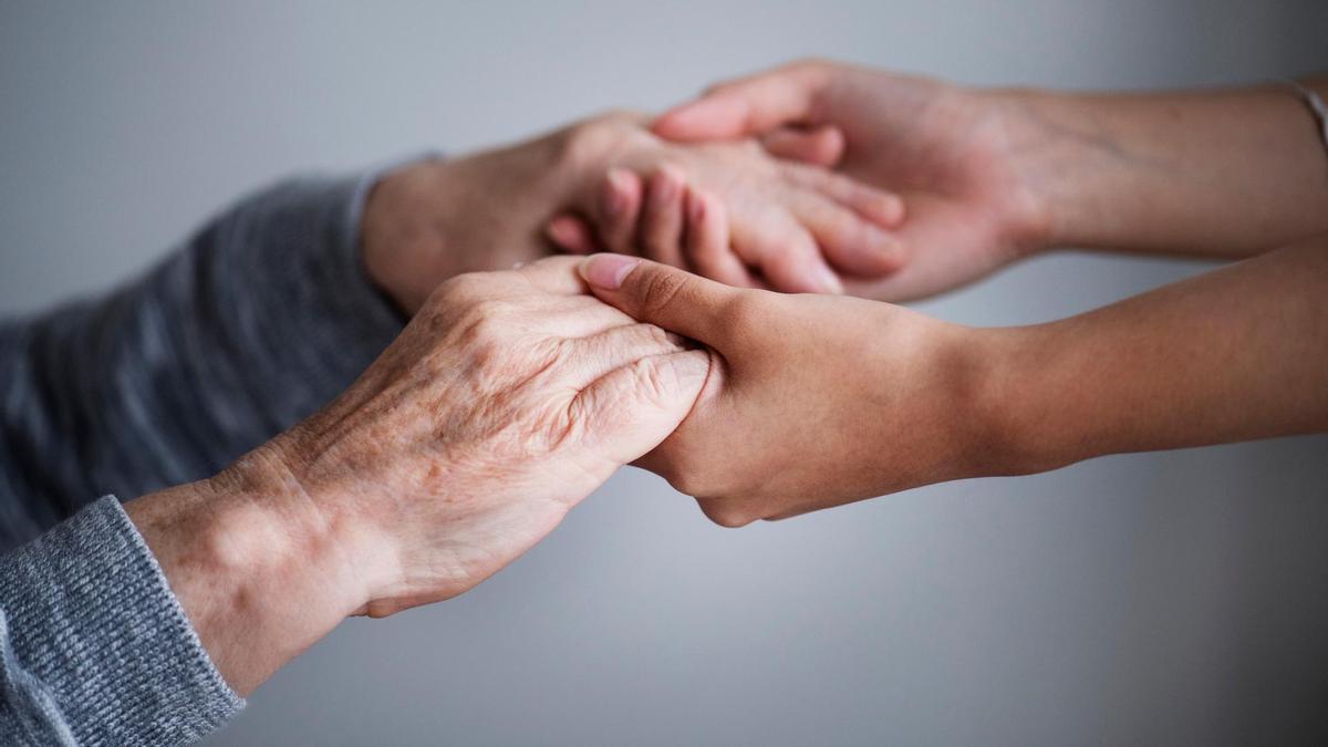 Las manos de una cuidadora prestan ayuda a una persona mayor.