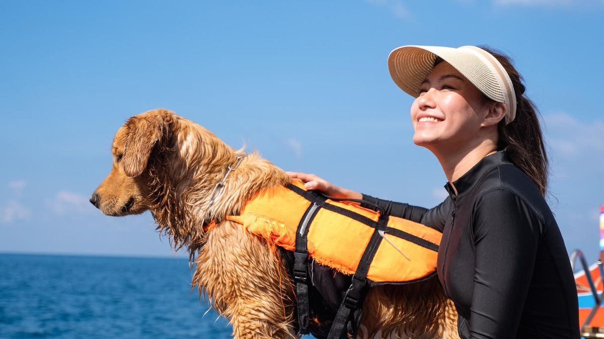 Una mujer y su golden retriever con chaleco salvavidas sentados en un bote.