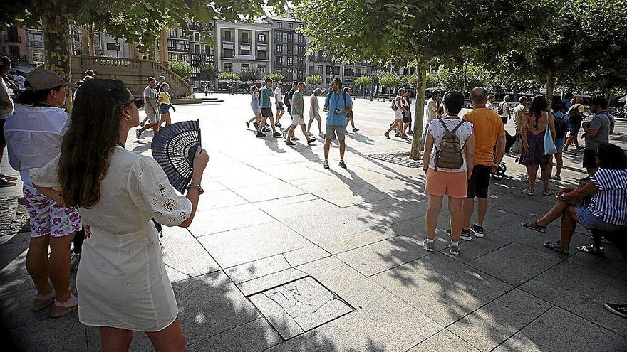 Un grupo de turistas escucha a la sombra las explicaciones de su guía ayer en la Plaza del Castillo, mientras otros visitantes cruzan por detrás.