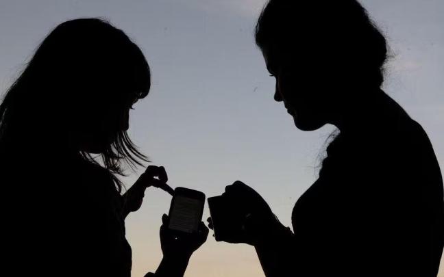 Dos jóvenes consultan un teléfono móvil Dos jóvenes consultan un teléfono móvil
