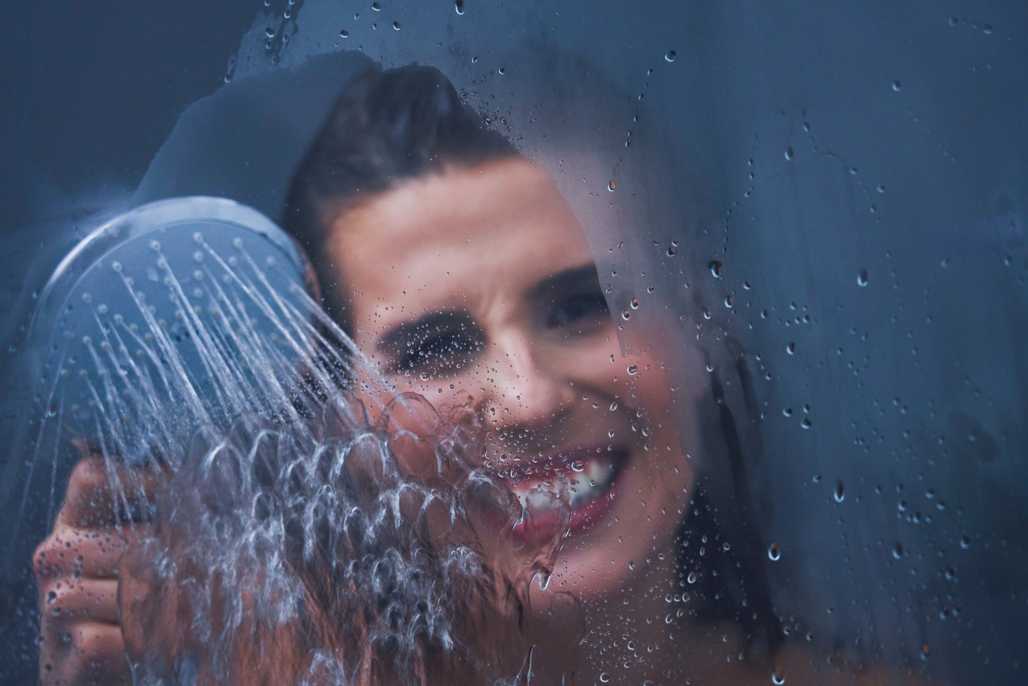 Una mujer moja un cristal empañado con la alcachofa de la ducha.