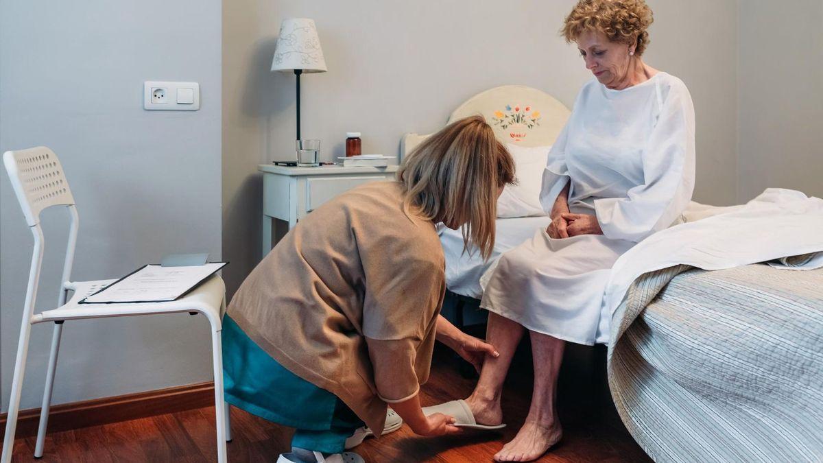 Una cuidadora ayuda a una mujer mayor a calzarse.