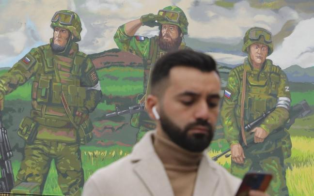 Un hombre observa su tel&eacute;fono en Mosc&uacute; ante un mural de las tropas rusas.
