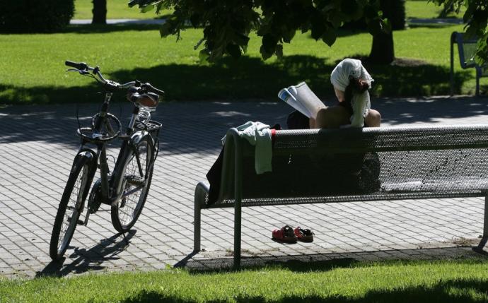 Una mujer leyendo una revista sentada en un banco junto a su bicicleta.