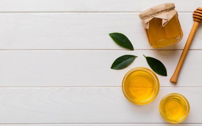 Recipientes con miel junto a una cuchara mielera.