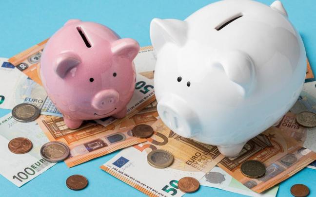 Monedas y billetes junto a dos huchas con forma de cerdito.